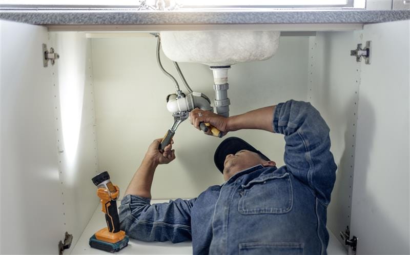 Plumber repairing pipes beneath a bathroom sink in Goleta